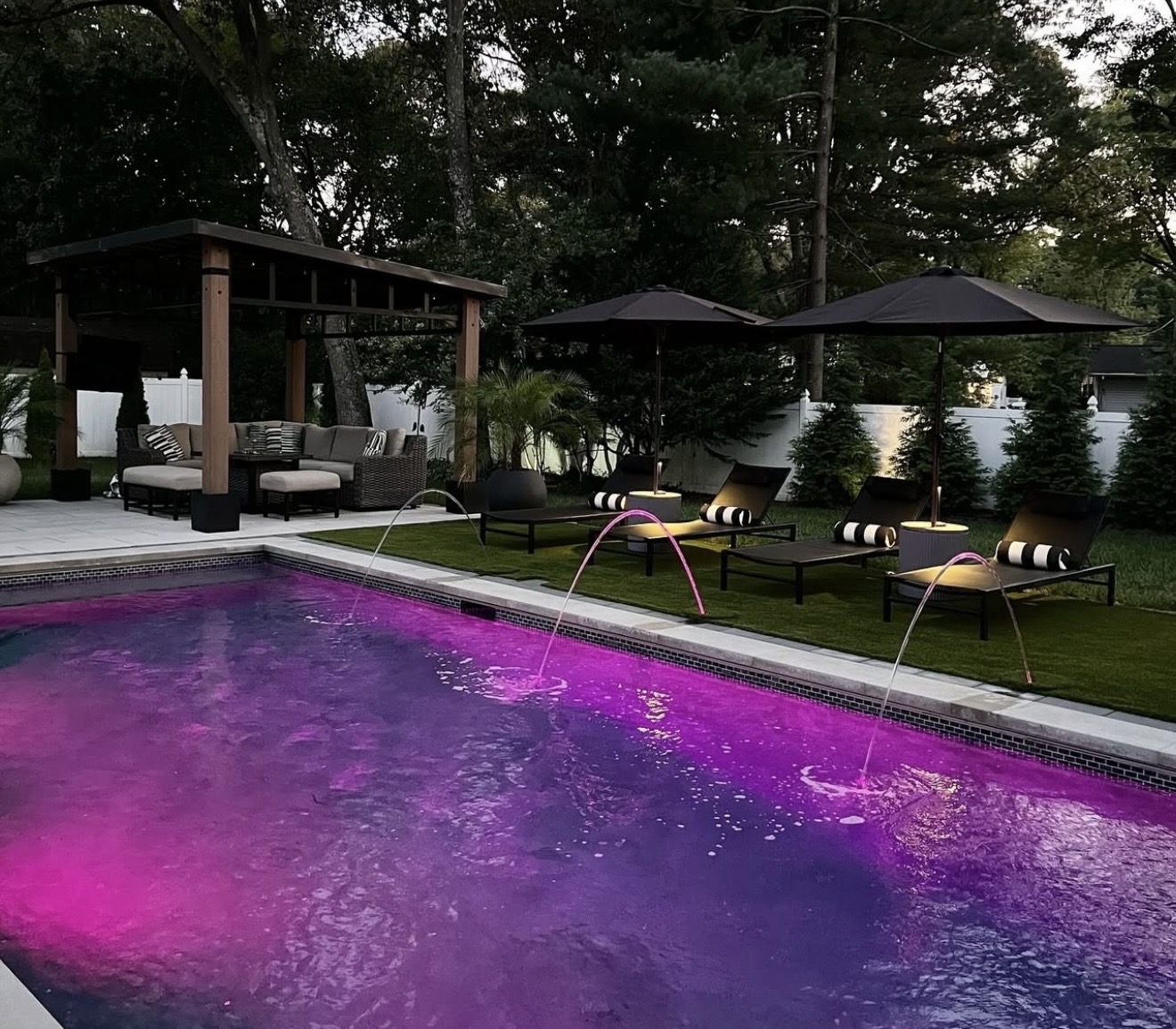 Custom shotcrete pool at dusk with color LED lighting, deck jets, and a covered pergola lounge in Littleton, Colorado